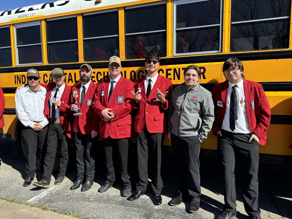 Six people in red and gray jackets pose in front of a yellow school bus.