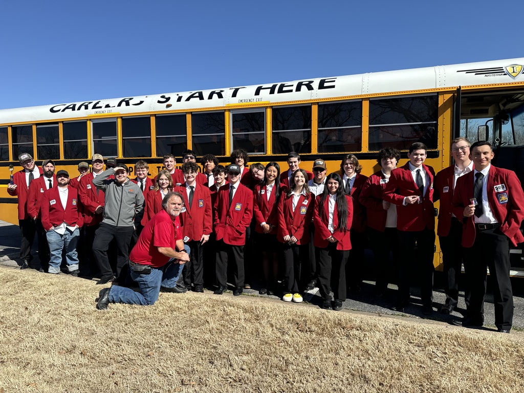 A group of people in red coats and ties, some kneeling, standing by a yellow bus with "Carl R. Start Here" on it.