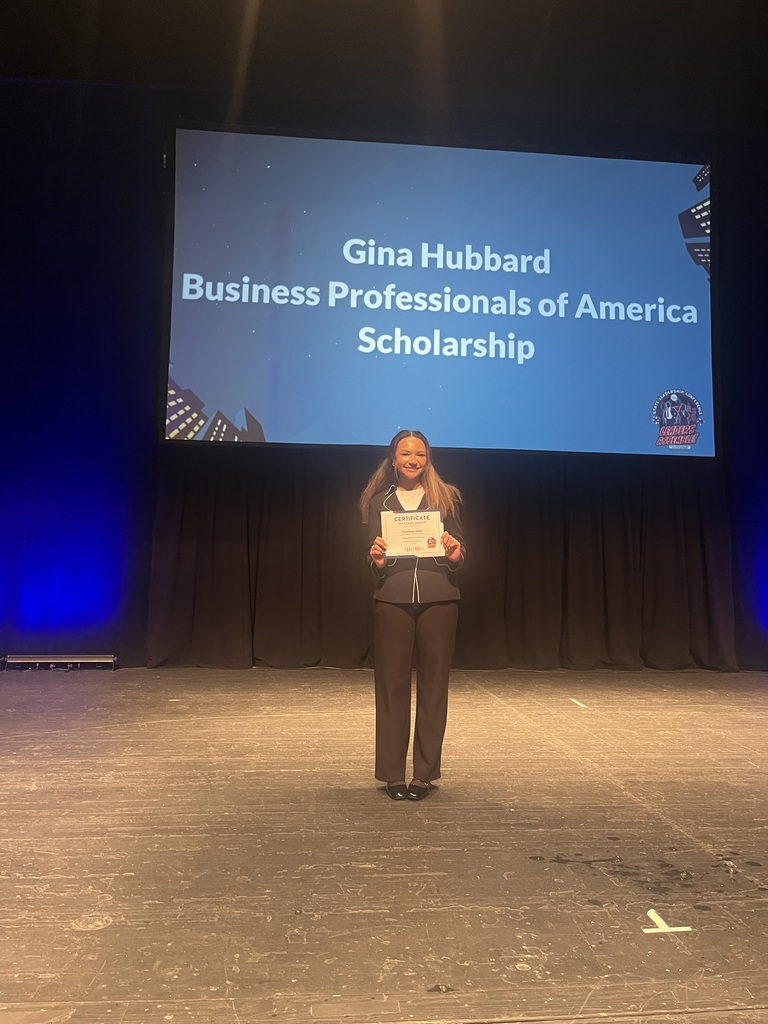 A person holds a certificate on a stage, with a large screen behind them displaying "Gina Hubbard Business Professionals of America Scholarship".