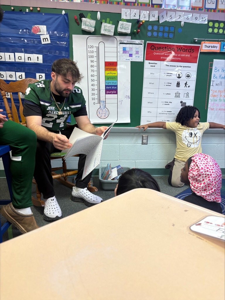 A Mercyhurst University Football player reading to students in a classroom.
