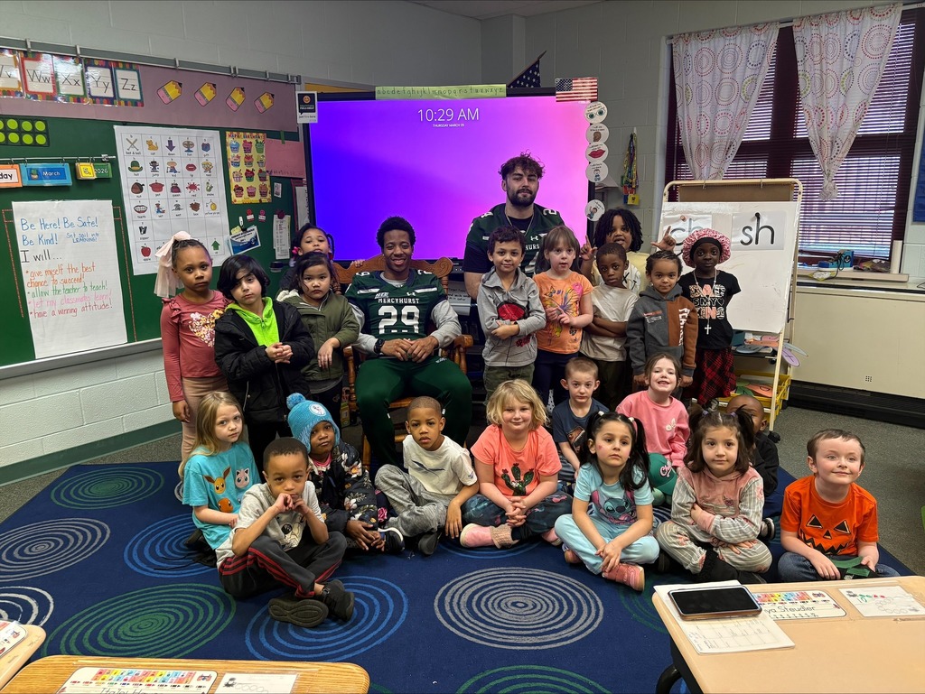 Students and a teacher standing next to Mercyhurst University Football Players in a classroom.