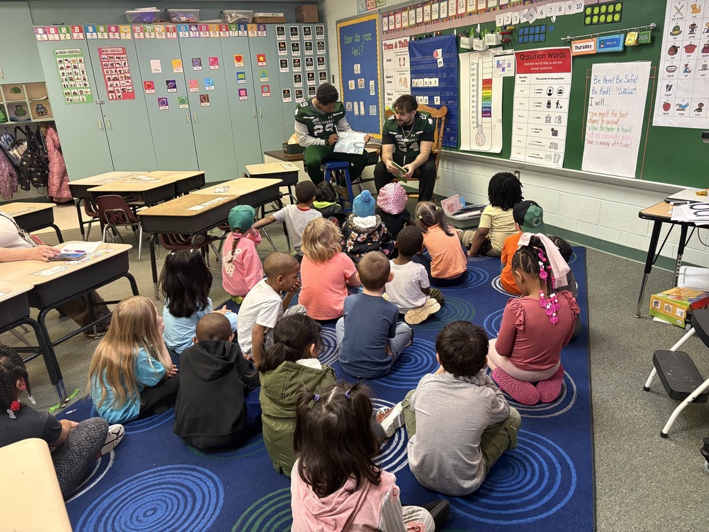 Mercyhurst University Football players reading to students in a classroom.