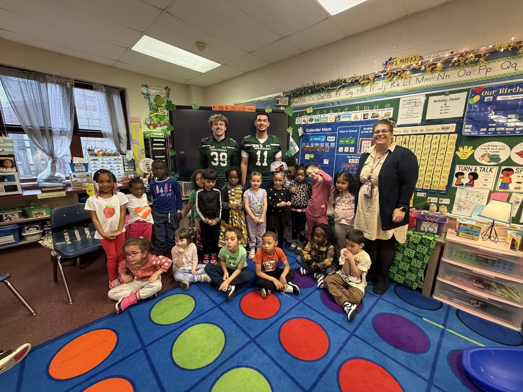 Students and a teacher standing next to Mercyhurst University Football Players in a classroom.