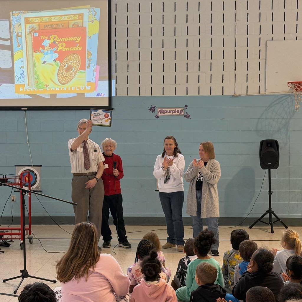 A man holding a certificate up in a school gym where students are sitting. 