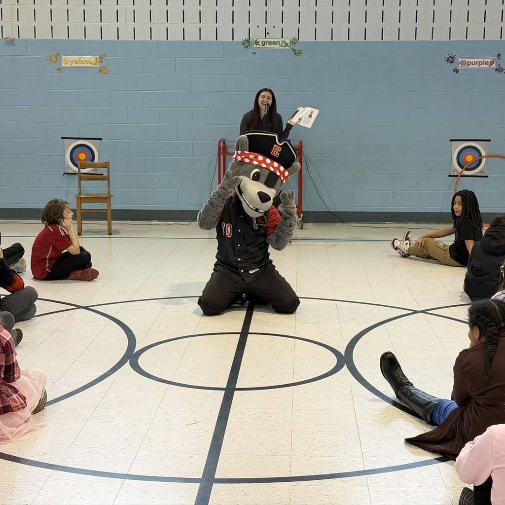 Erie SeaWolves Mascot acting in front of kids as a young lady reads behind him. 
