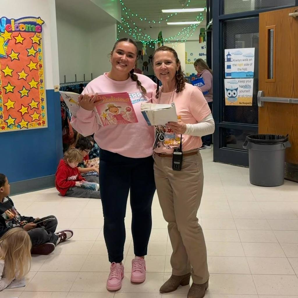 Two teachers dressed in pink and they are holding books they are reading. 