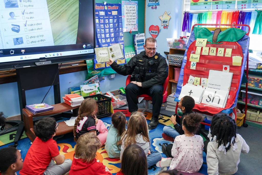 A school security officer is reading a book to kids in a classroom. 