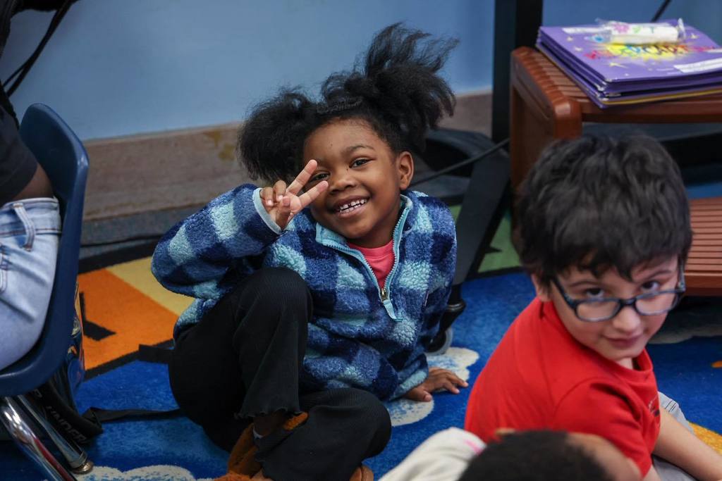 A young girl smiling and holding up a peace sign. 