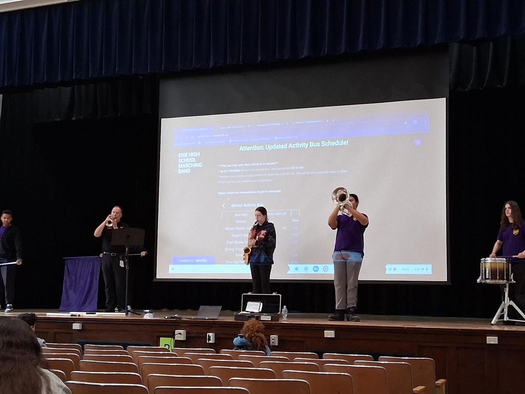 The Erie High School marching band performing in an auditorium where students are sitting and watching.