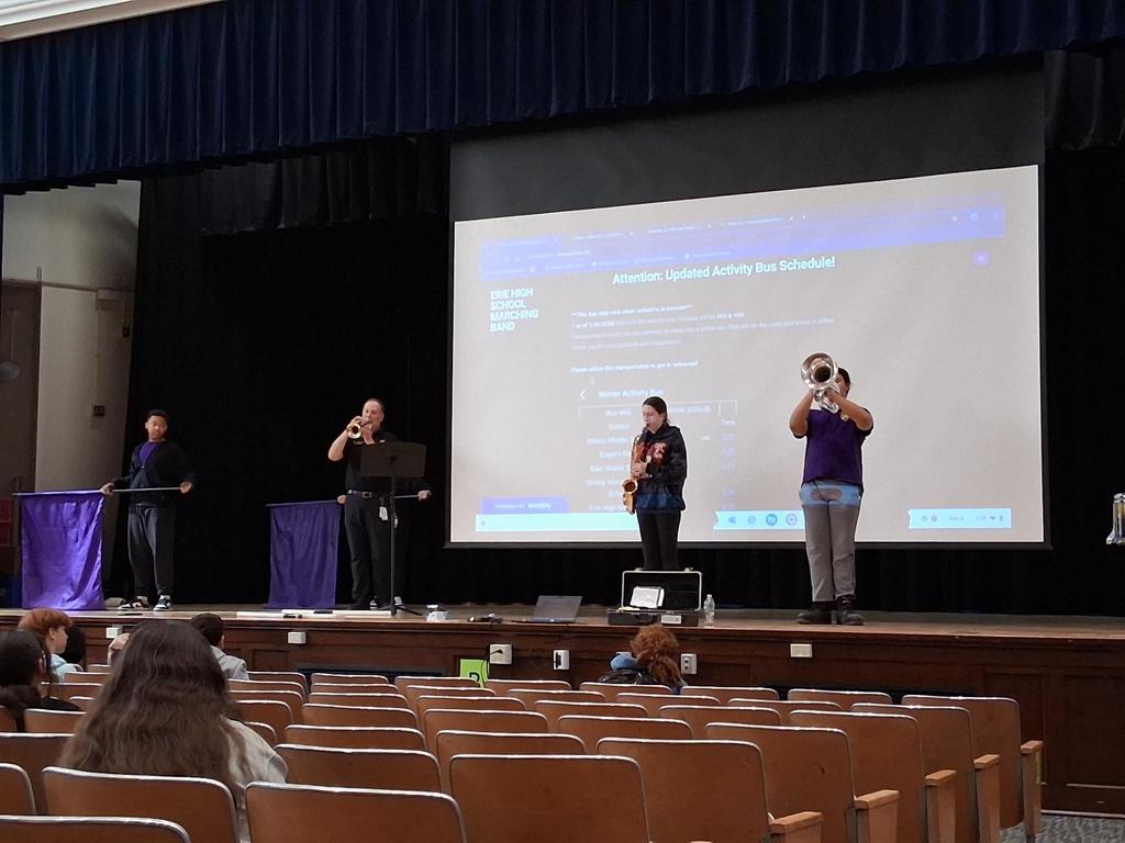 The Erie High School marching band performing in an auditorium where students are sitting and watching.