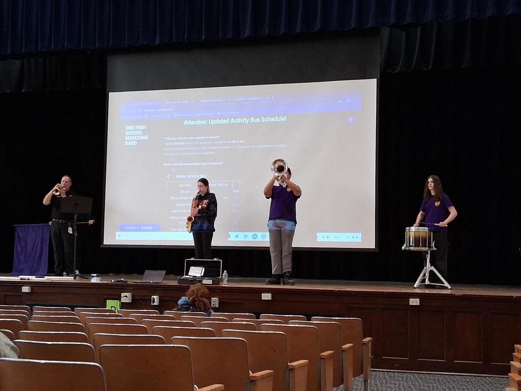 The Erie High School marching band performing in an auditorium where students are sitting and watching.