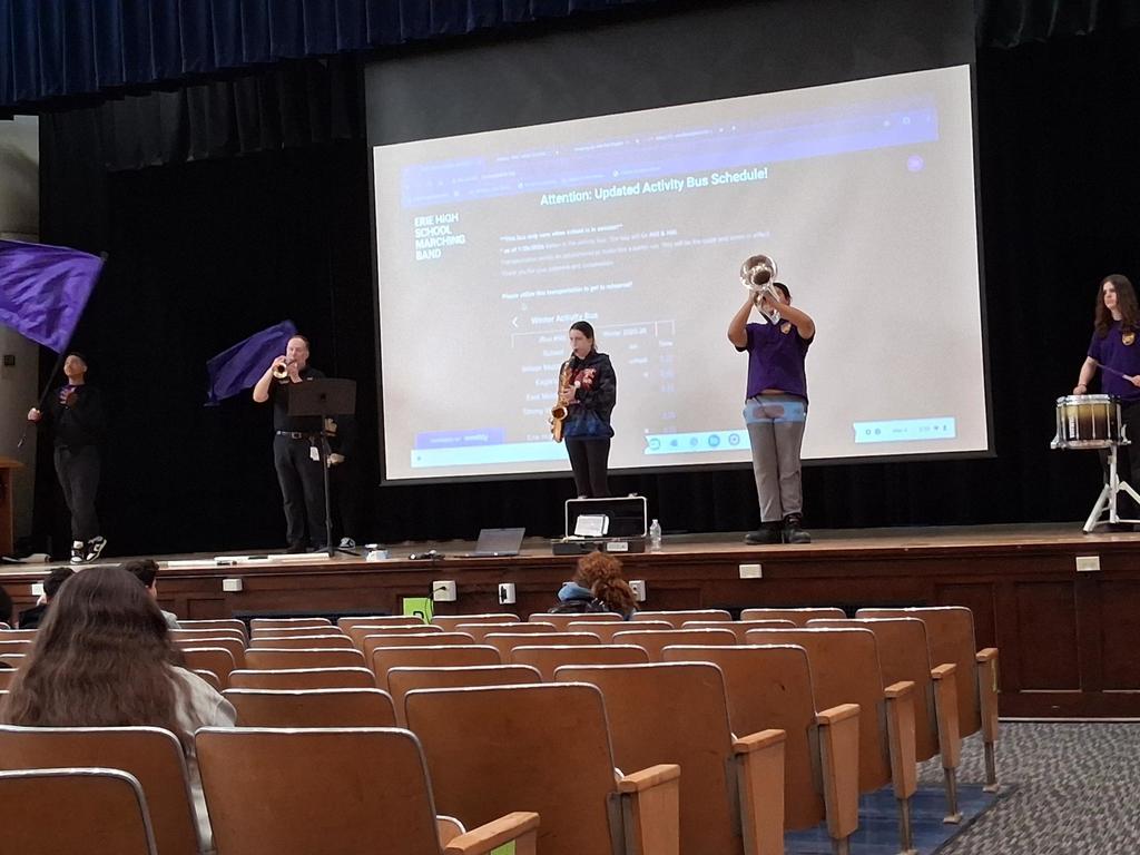 The Erie High School marching band performing in an auditorium where students are sitting and watching.