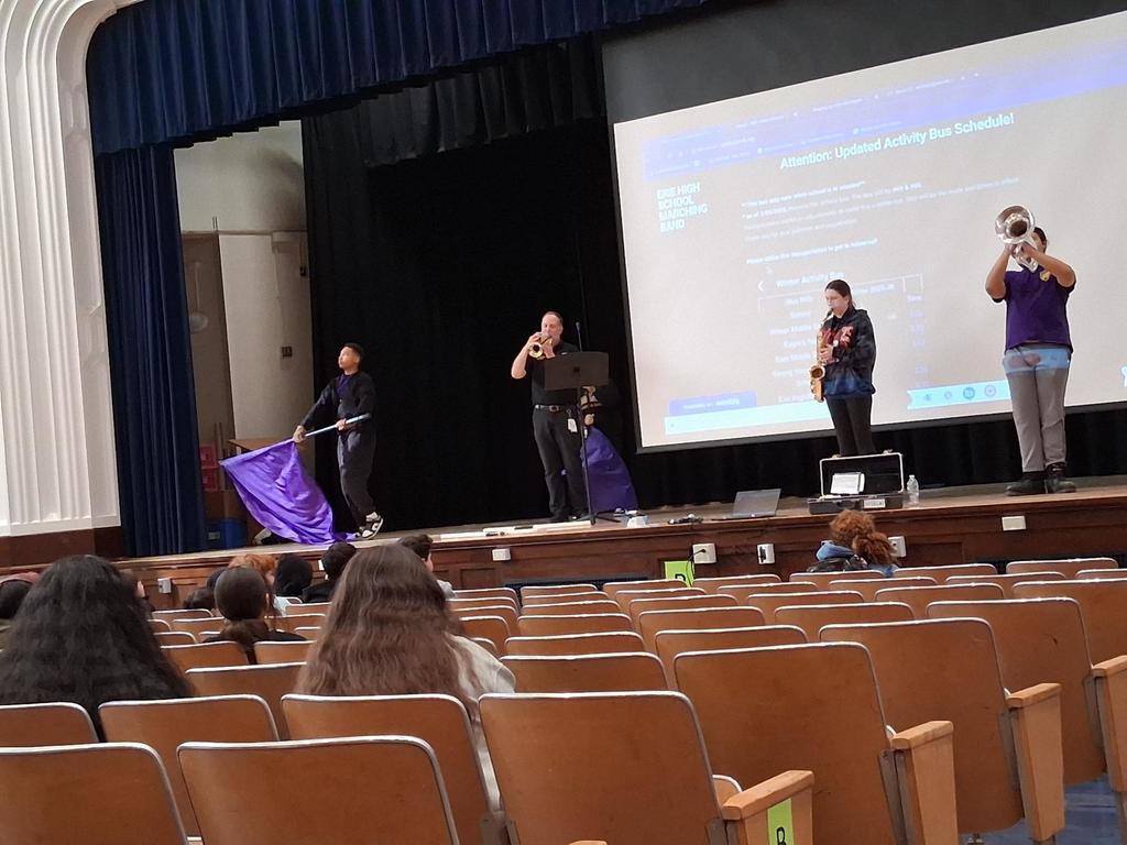 The Erie High School marching band performing in an auditorium where students are sitting and watching.