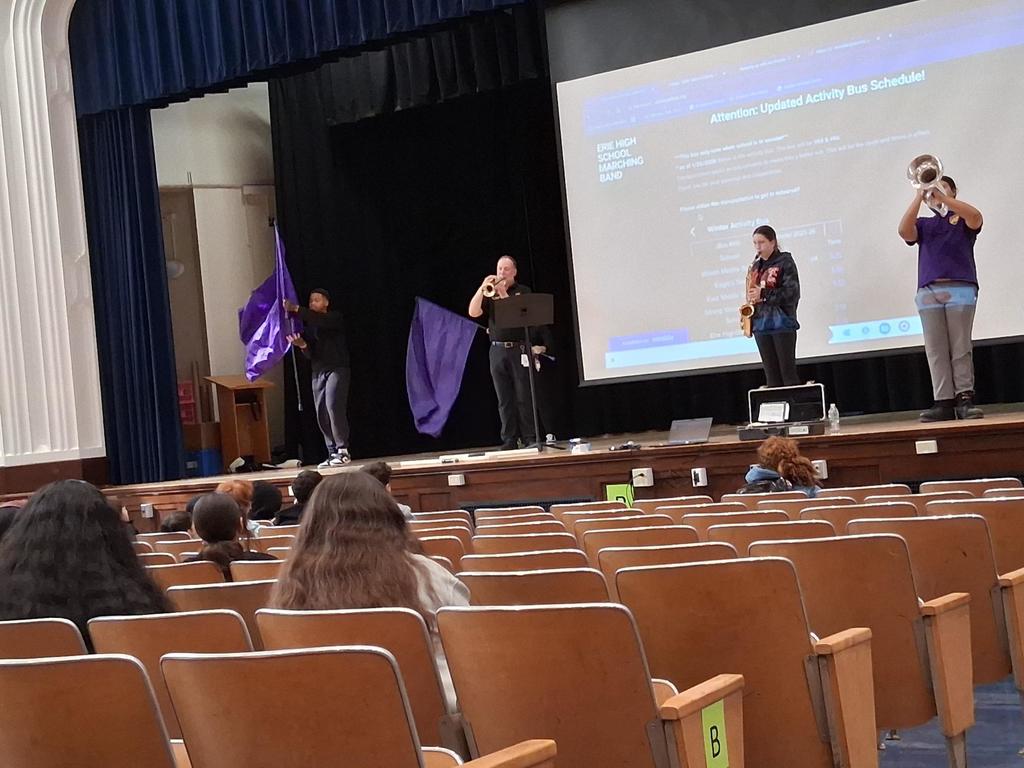 The Erie High School marching band performing in an auditorium where students are sitting and watching.
