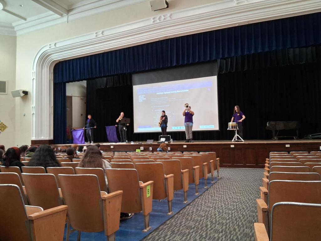 The Erie High School marching band performing in an auditorium where students are sitting and watching.
