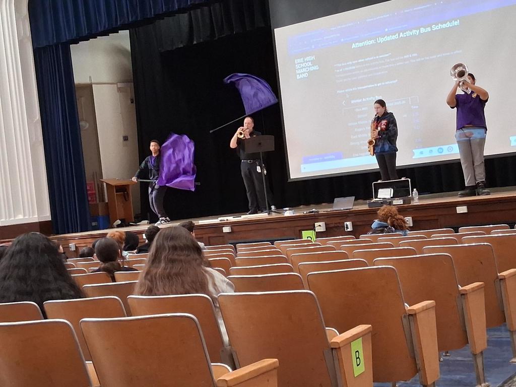 The Erie High School marching band performing in an auditorium where students are sitting and watching.