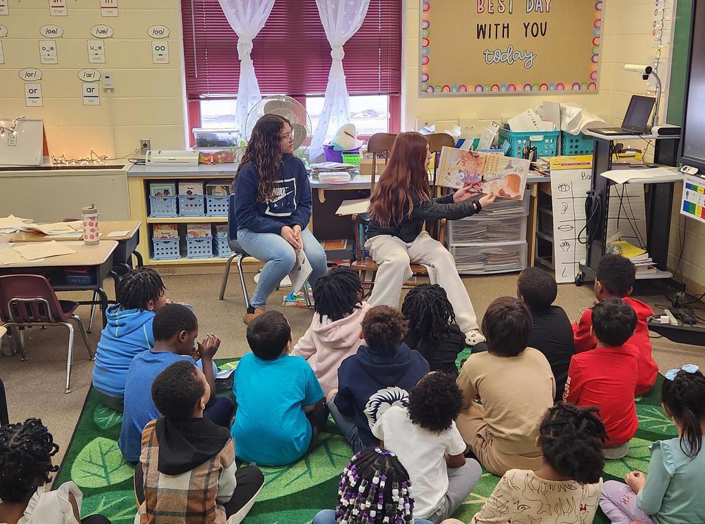A student reading to a classroom of younger students.