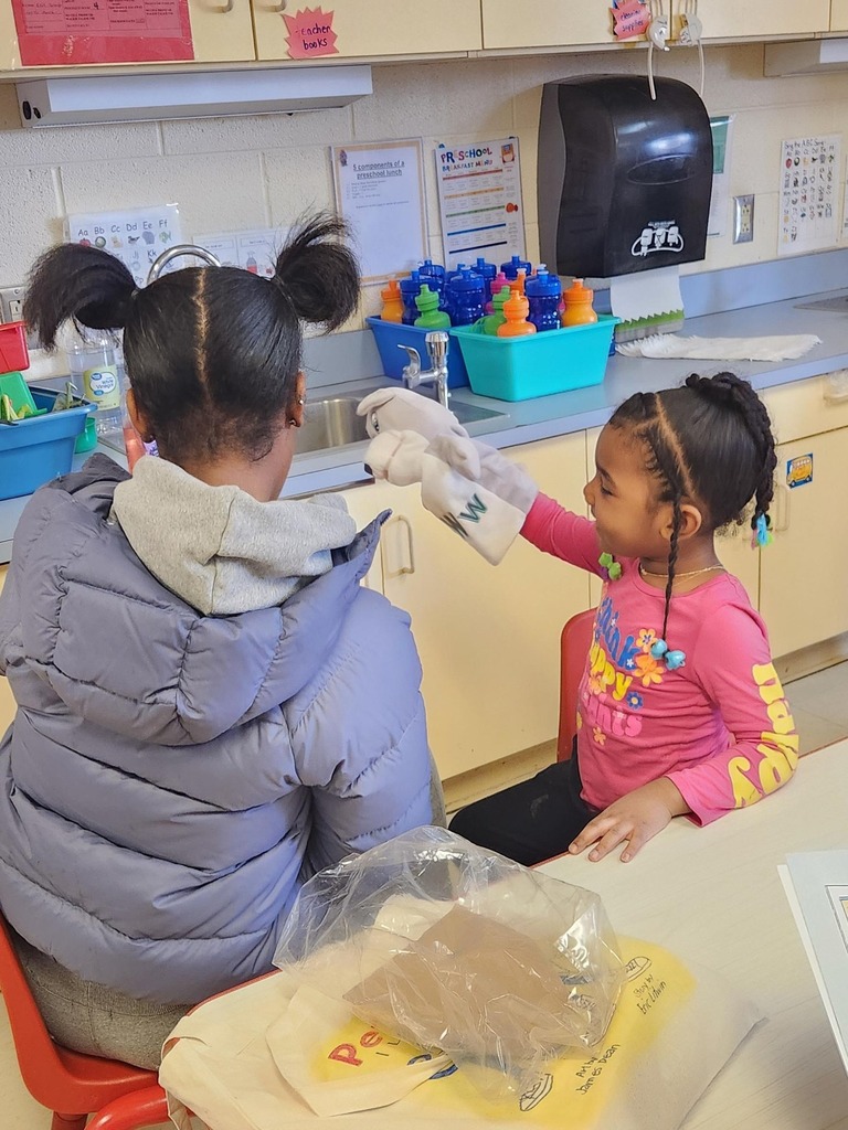 A student reading to a younger kid. who is holding a puppet.