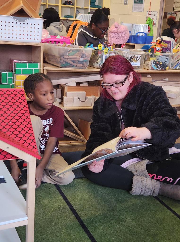 A student reading to a younger kid.