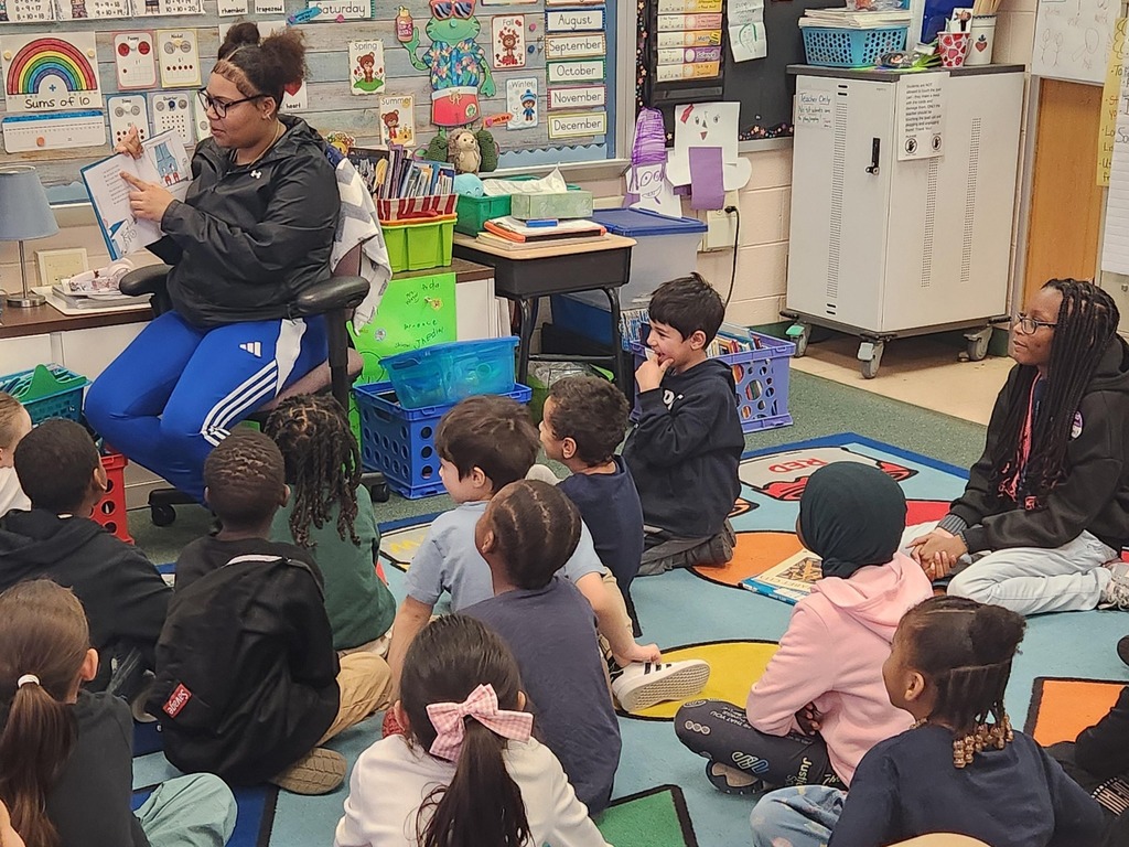A student reading to a classroom of younger students.