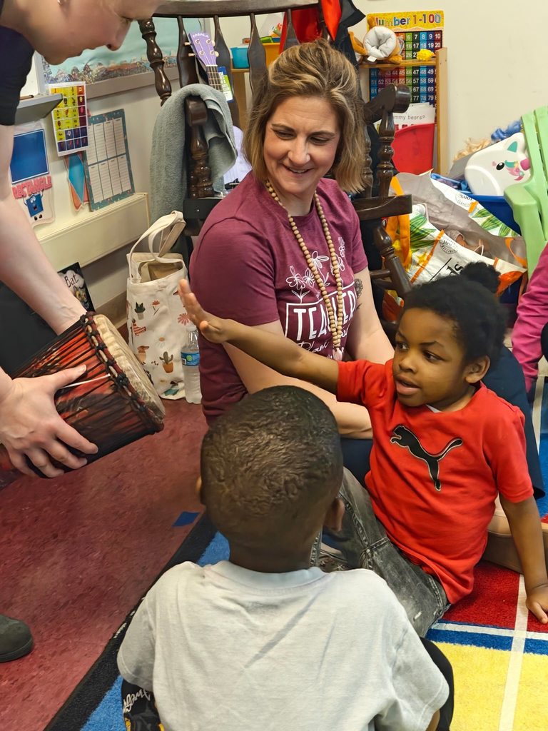 A student playing a drum that someone is holding.