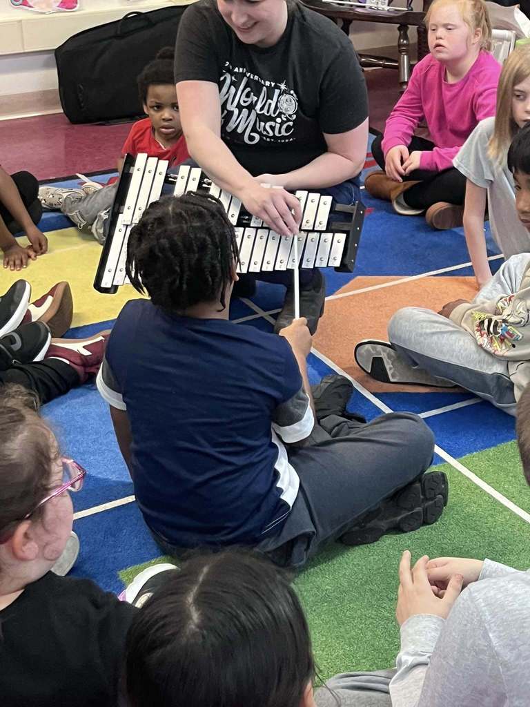 A teacher holding a xylophone and a student playing it. 