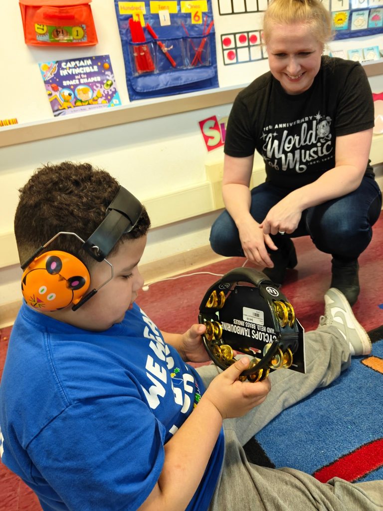 A student playing a tambourine and he is wearing headphones. 