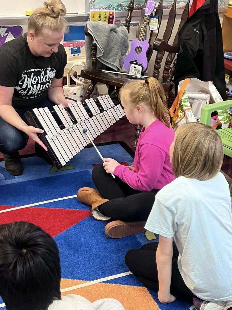 A teacher holding a xylophone and a student playing it. 