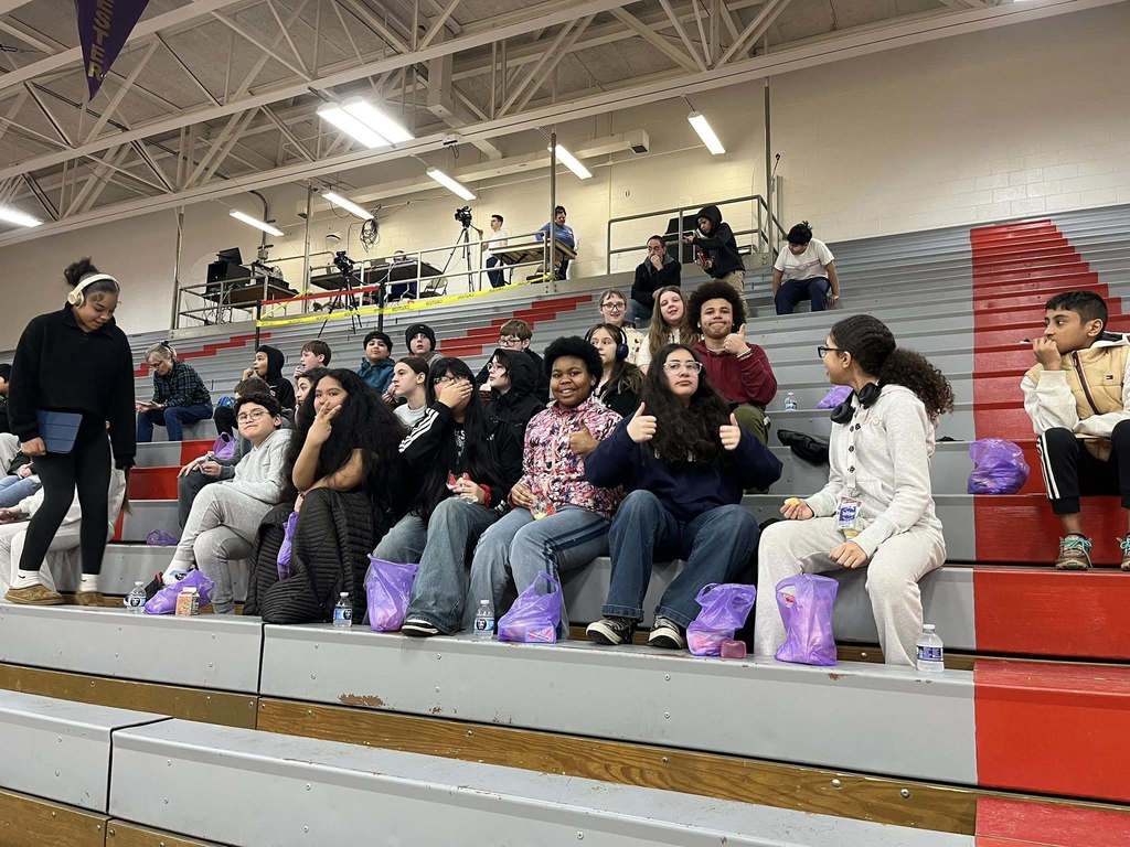 Students sitting on bleachers and putting up peace signs and thumbs up.