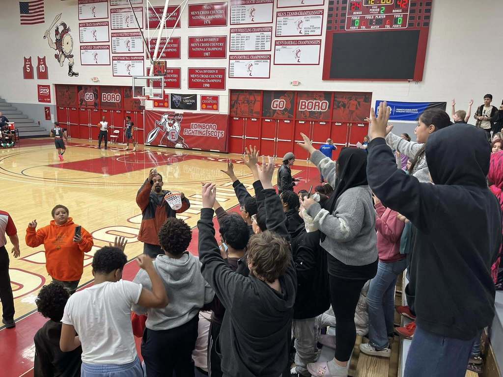 People holding their hands out to get something that is being passed out from the basketball court.