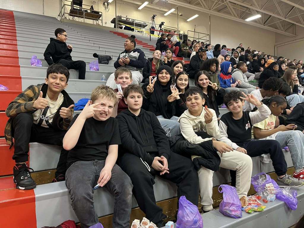 Students sitting on bleachers and putting up peace signs and thumbs up.