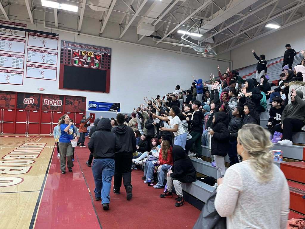 People holding their hands out to get something that is being passed out from the basketball court.