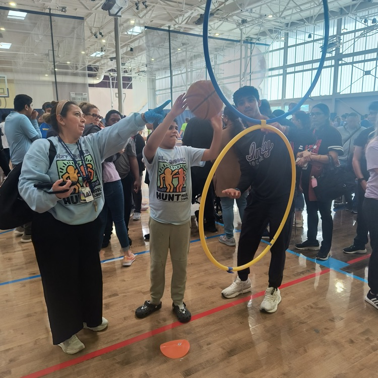 Teacher and volunteer holding hula hoop as student puts basketball through it