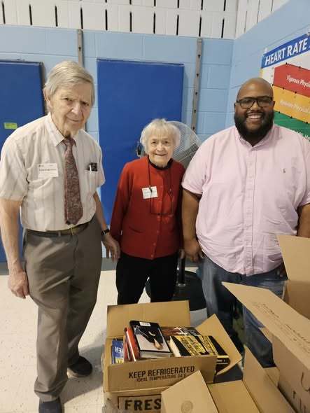 Two elderly individuals standing with a man in a polo shirt. 