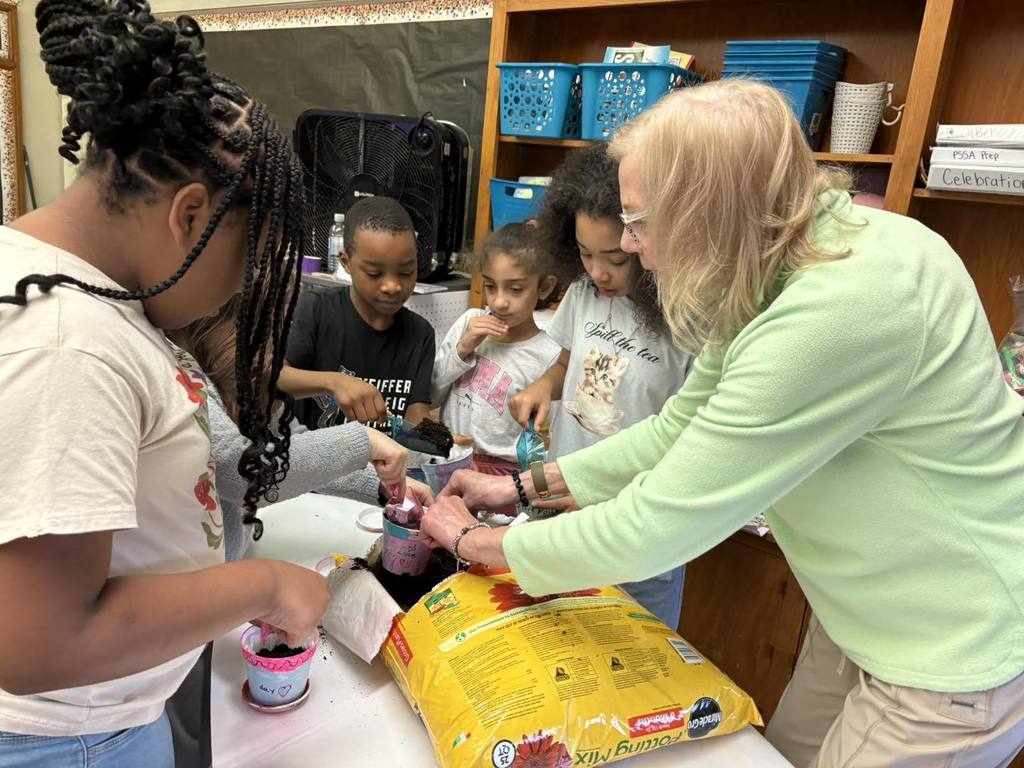 A women helping students put dirt in their containers. 