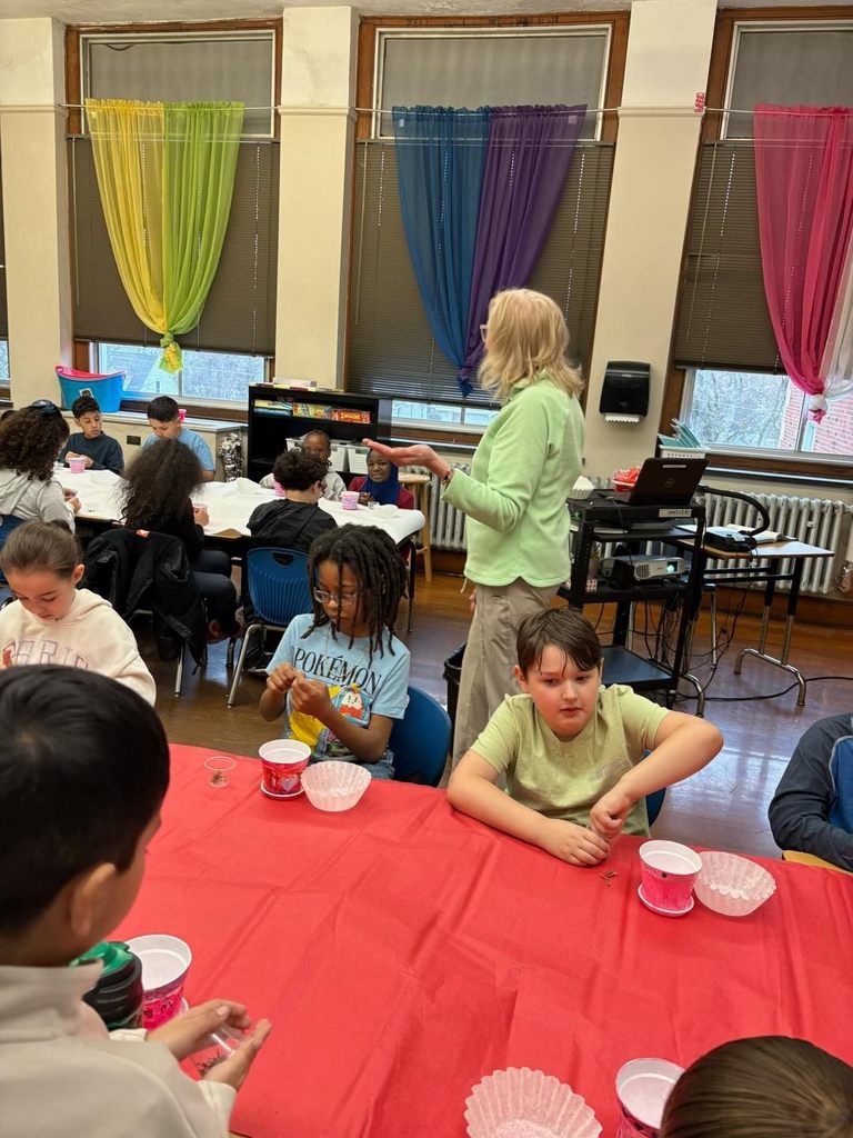 A teacher talking to a classroom of students who are planting seeds in a container. 