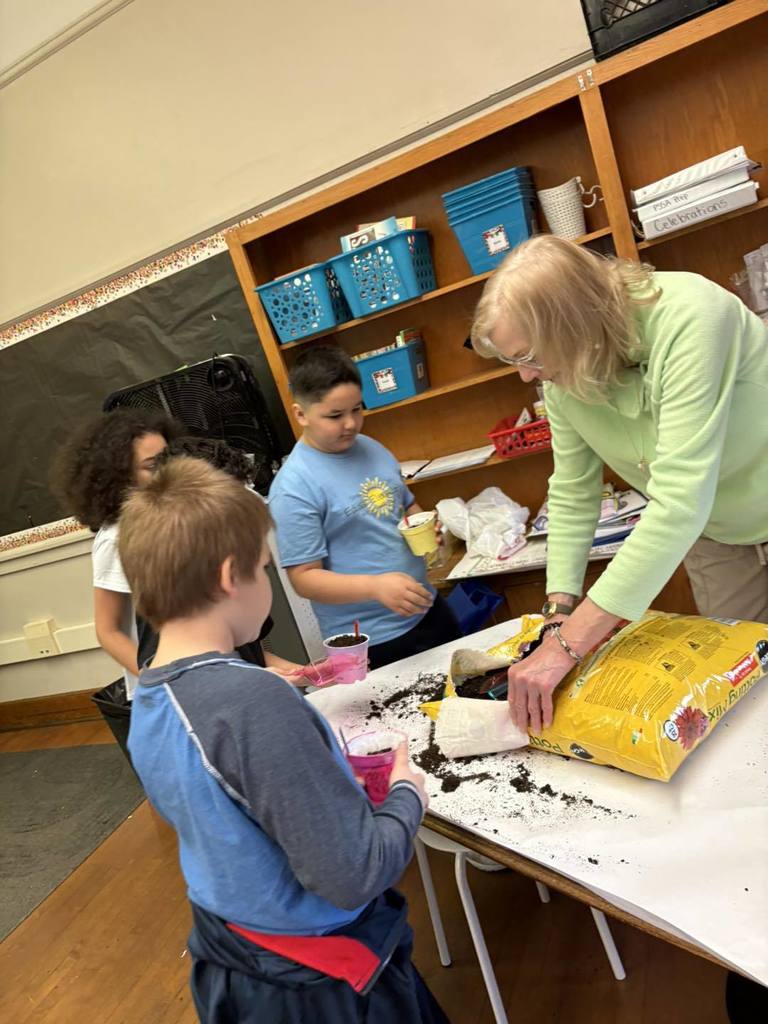 A women helping students put dirt in their containers. 