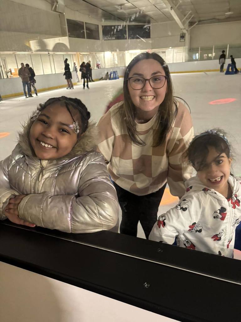 An adult and students smiling on the ice rink. 