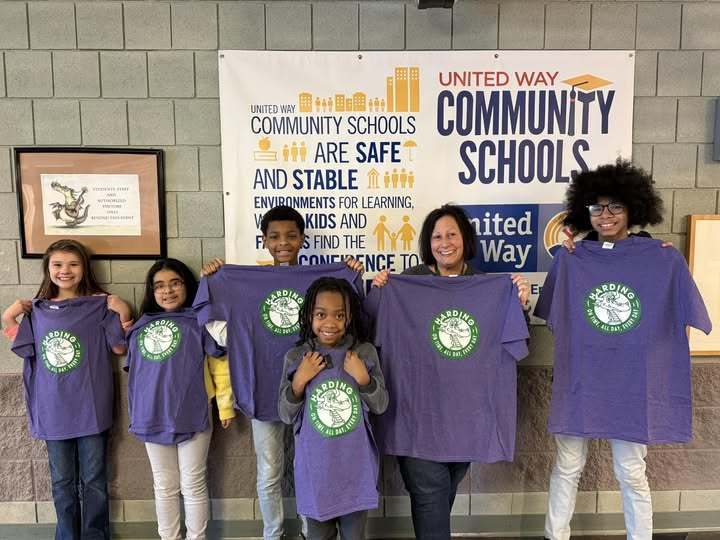 A teacher and students holding matching purple shirts with a Harding elementary school logo on it. 