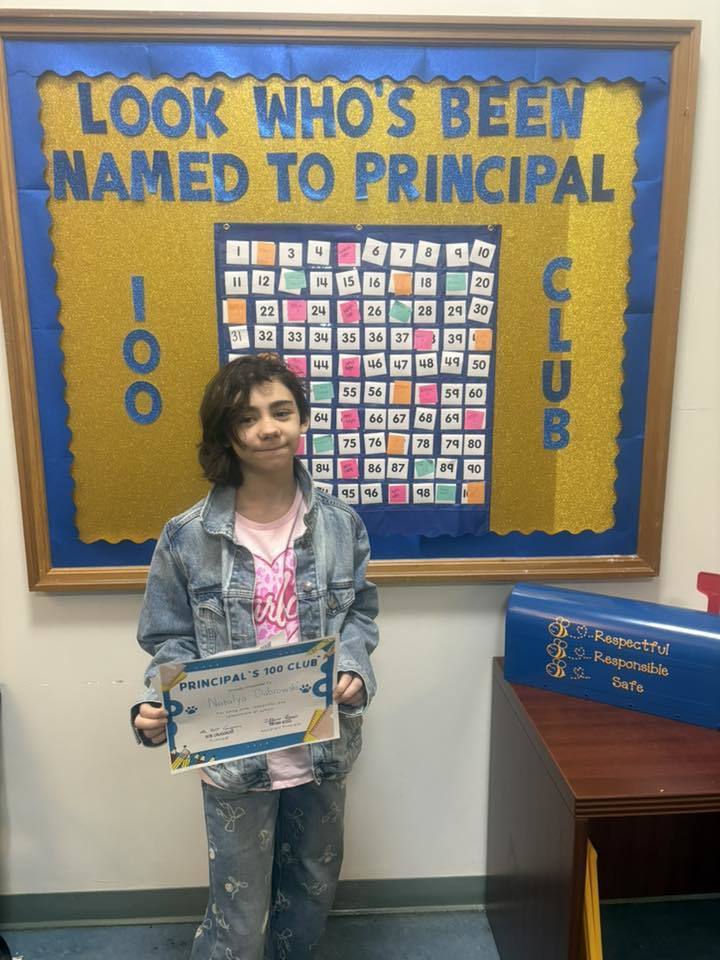 A student holding their "Principal 100 Club" certificate. 