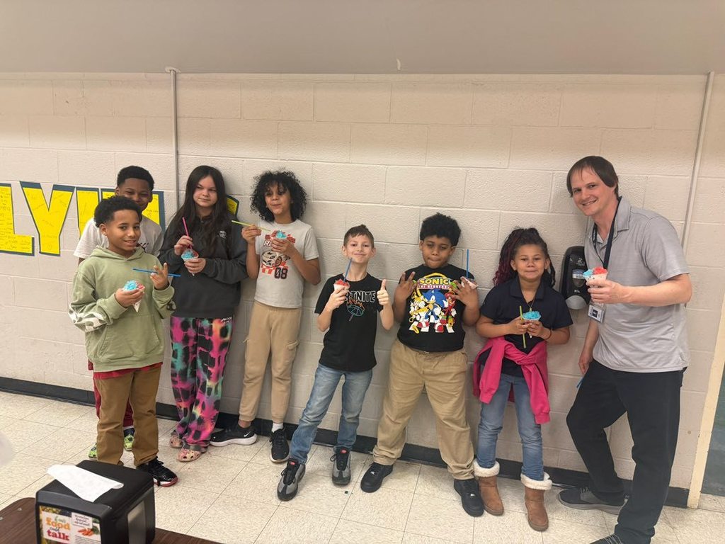 Students and teacher smiling in a hall and holding their snow cones. 