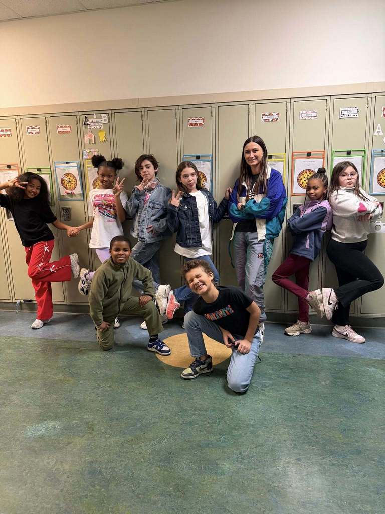 Students and teacher dressed like they are in the 80s and are posing in front of lockers. 