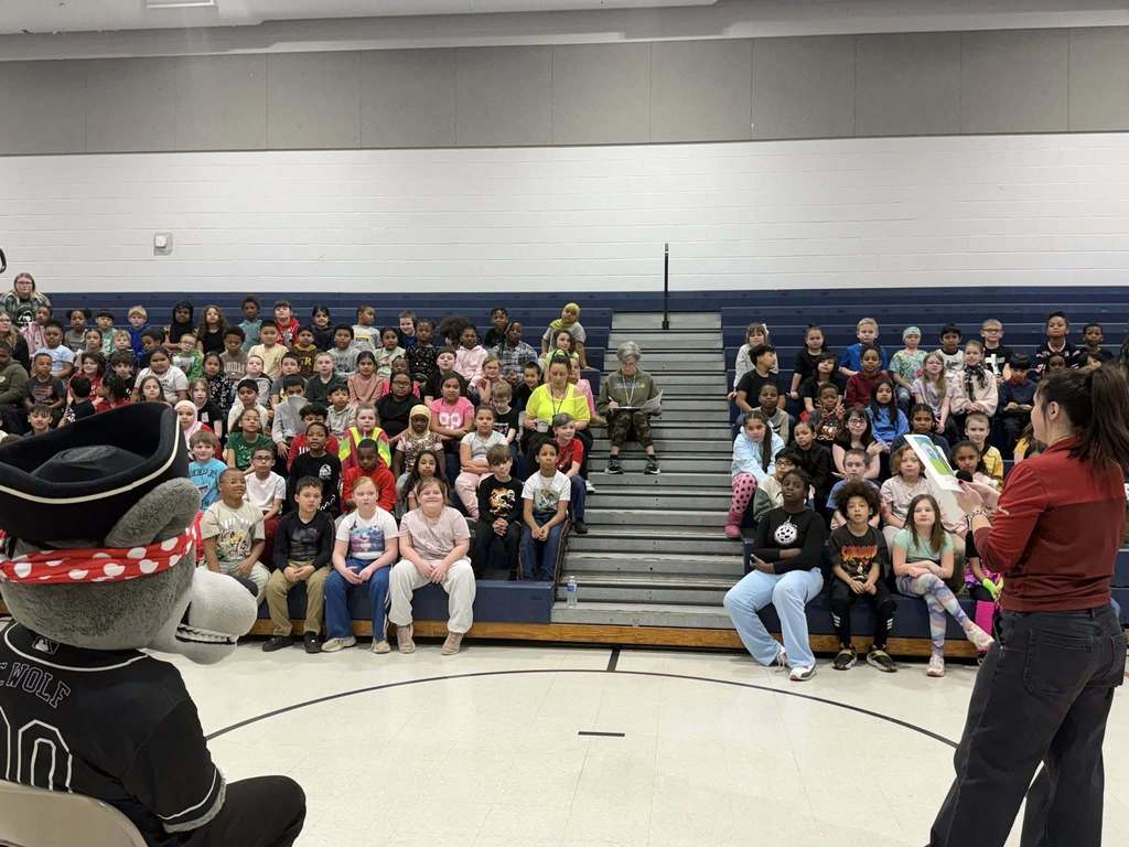 Students and teachers sitting on bleachers while the Erie SeaWolves mascot sits in front of them on a chair. 