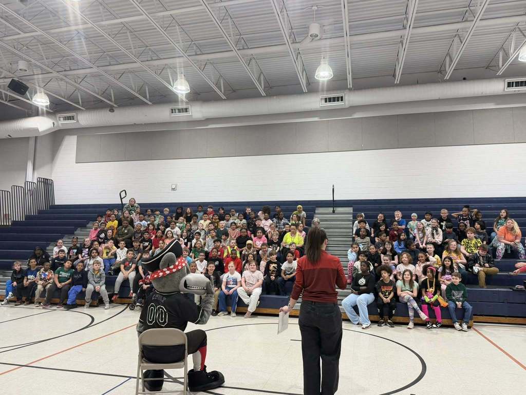 Students and teachers sitting on bleachers while the Erie SeaWolves mascot sits in front of them on a chair. 