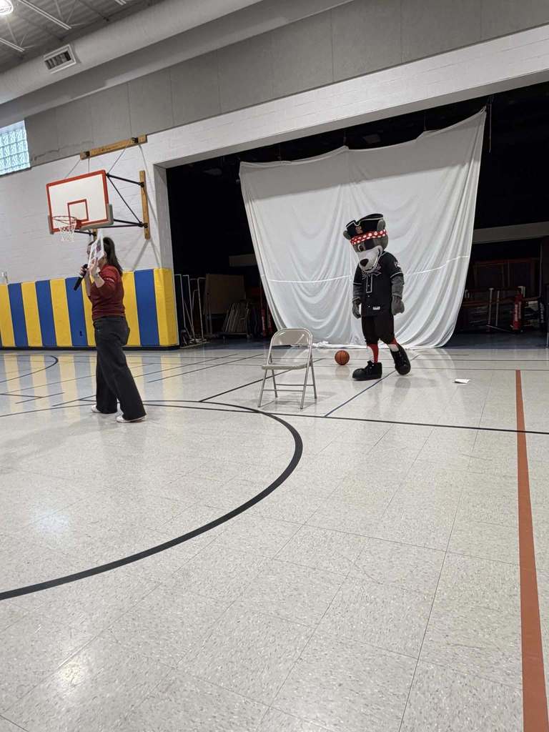 Women speaking while the Erie SeaWolves Mascot stands on the basketball court. 
