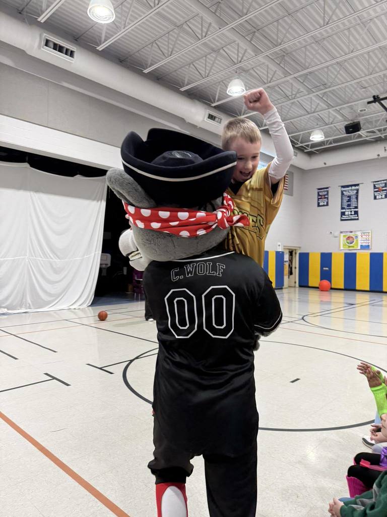 The Erie SeaWolves mascot holding a kid who is cheering. 
