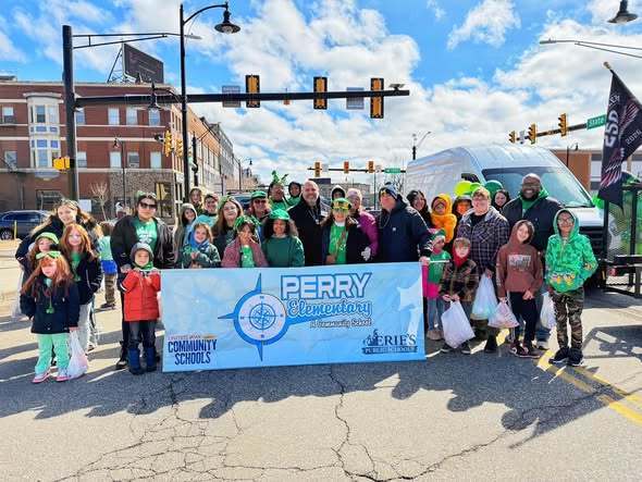 Kids and adults holding a banner that has the Perry Elementary School logo on it for a parade. 