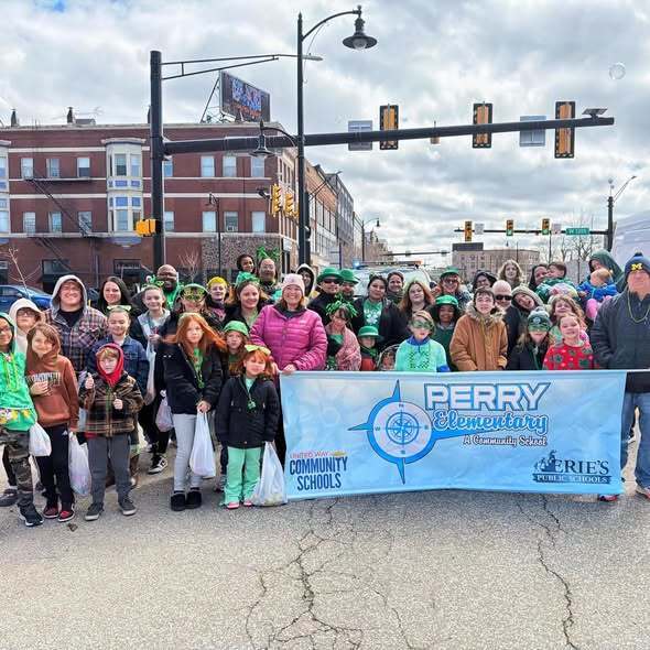 Kids and adults holding a banner that has the Perry Elementary School logo on it for a parade. 