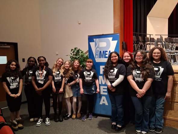 Students in black matching shirts standing next to a P.M.E.A. sign and smiling. 