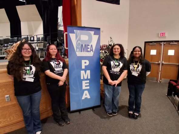 Students in black matching shirts standing next to a P.M.E.A. sign and smiling. 